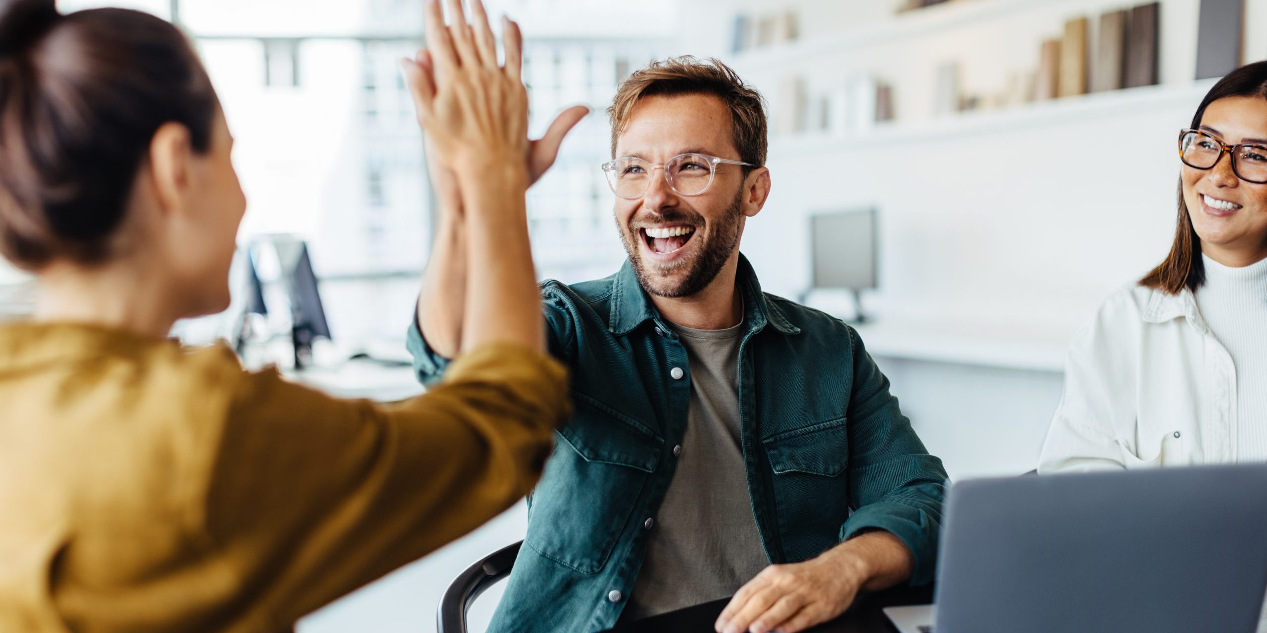 Successful business people giving each other a high five in a meeting. Two young business professionals celebrating teamwork in an office.